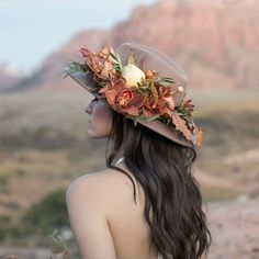 a woman wearing a hat with flowers on it's head in front of mountains