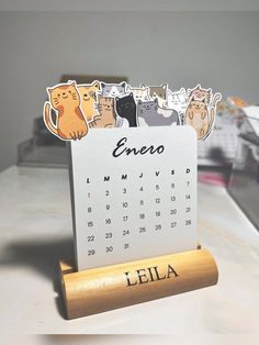 a desk calendar sitting on top of a wooden stand with cats drawn on the front