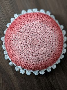 a pink and white crocheted round cushion on a wooden floor with lace trim