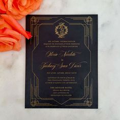 an elegant black and gold wedding card with orange flowers on the table next to it