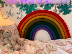 a stuffed animal sitting on top of a bed next to a rainbow wall hanging above it