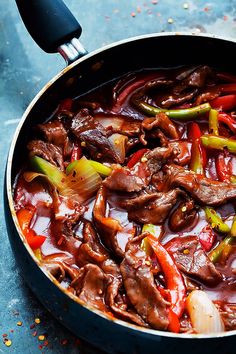 a pot filled with beef and peppers on top of a blue countertop next to a spatula