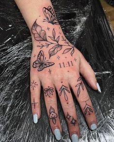 a woman's hand with tattoos on it and butterflies in the middle of her fingers