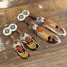 four native american style earrings with feathers and beadwork on wooden table next to earring hooks