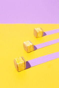 three pieces of cake sitting on top of purple and yellow paper with sticks sticking out of them