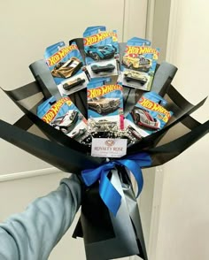 a person holding a bunch of hot wheels toys in their hand with blue ribbon around it