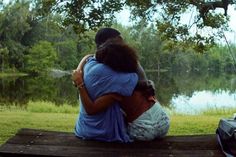 a man and woman sitting on a bench next to a lake