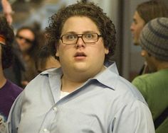 a man with glasses is standing in front of a group of people on the subway