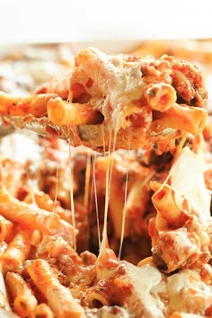 a fork full of pasta being lifted from a casserole dish with meat and cheese