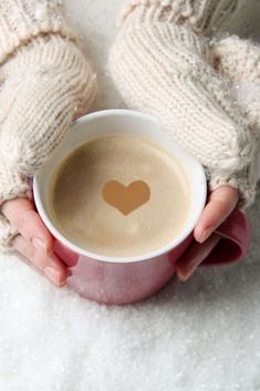 a woman holding a cup of coffee with a heart drawn on the foam in her hands