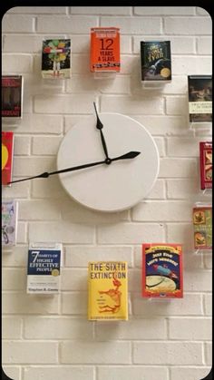 a white clock mounted to the side of a brick wall with books on it's sides