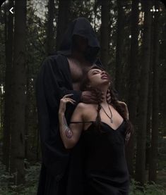 a woman in a black dress is hugging a man in a hooded hood and cloak