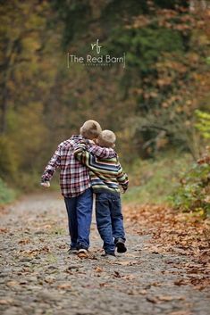 two young boys walking down a dirt road in the woods with their arms around each other