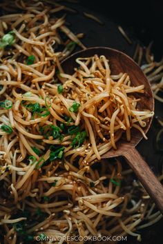 a wooden spoon filled with pasta and parsley on top of a black pan full of noodles