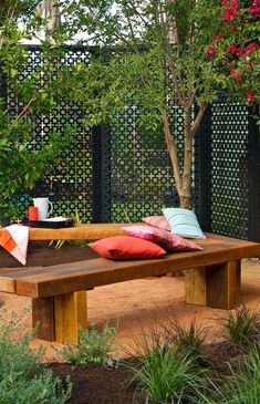 a wooden bench sitting in the middle of a garden with pillows on top of it