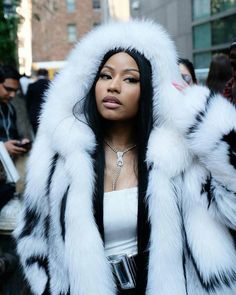 a woman with long black hair wearing a white and black fur coat on the street