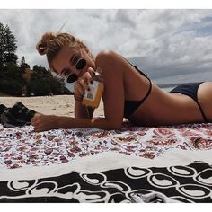 a woman laying on top of a beach next to a blanket and holding a bottle