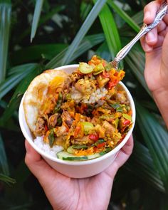 someone is holding a bowl of food with rice and vegetables in it while another hand holds a spoon