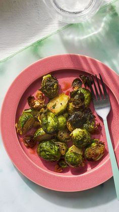 a pink plate topped with brussel sprouts next to a fork