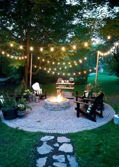 a fire pit surrounded by chairs and lights in the middle of a yard with lots of greenery