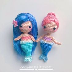 two crocheted mermaid dolls sitting next to each other on a white surface with pink and blue hair