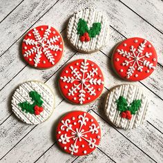 four decorated cookies sitting on top of a white wooden table with snowflakes and holly