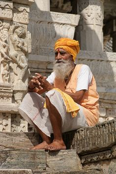 an old man with a yellow turban sitting on some steps