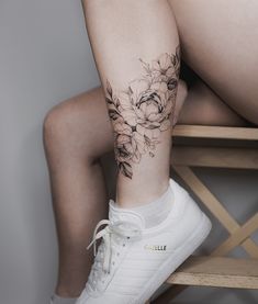 a woman's leg with flowers on it and a white tennis shoe sitting next to her