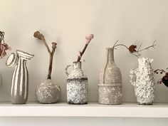 five vases are lined up on a shelf with flowers and branches in the middle