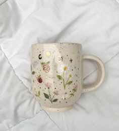 a white coffee cup with flowers painted on the side and stars in the middle, sitting on a bed