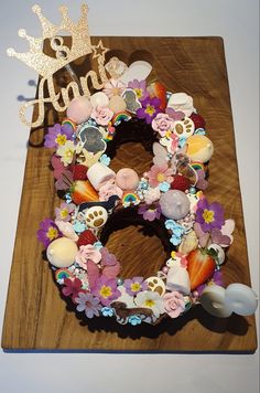 a wooden cutting board topped with a flower wreath and a cake topper that says queen