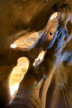 a person climbing up the side of a rock formation in a canyon with sunlight streaming through it