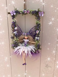 a purple and white fairy doll hanging from a door frame with flowers on it's side