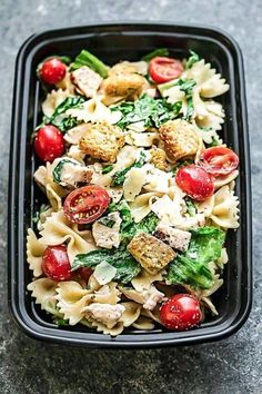 a black container filled with pasta and veggies on top of a stone table