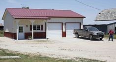 a truck parked in front of a two car garage on a dirt road next to a barn