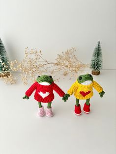 two crocheted frog dolls holding hands in front of christmas trees and garlands