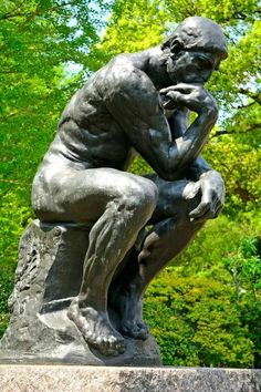 a statue of a man sitting on top of a stone slab in front of trees