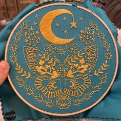 a person holding up a blue and yellow embroidered pillow with an image of the moon on it