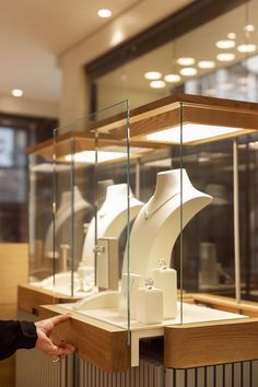 a woman is pointing at some white vases in a glass display case with lights above them