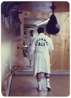 a man in a white coat and socks walking into a room with boxing gloves hanging from the ceiling