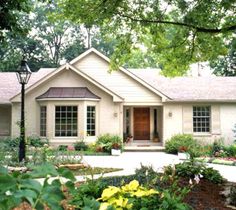 a white house with red front door and black shutters on the windows is surrounded by greenery