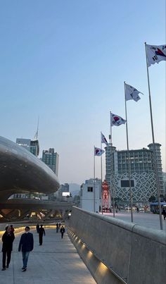 people walking on the sidewalk in front of some tall buildings and flags flying from them