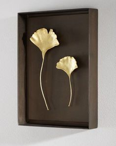 two metal flowers mounted on a wall in a black frame with gold leaf accents and a white background