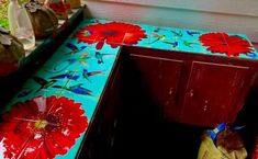 a wooden bench painted with red flowers on blue ground next to a door and window