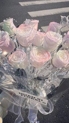 a clear vase filled with pink and white roses on top of a table next to a crosswalk