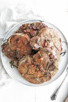 a white plate topped with meat covered in sauce and garnished with herbs next to a fork