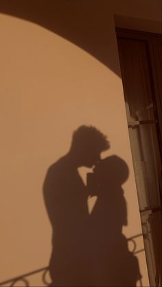 the shadow of a man and woman kissing in front of a building with a balcony