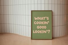 a green sign that says what's cooking good looking? in front of a tiled wall