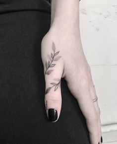 a woman's left hand with a small tattoo on the middle finger and an olive branch