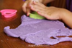 a young child is playing with purple play dough on a table next to a pink plastic container